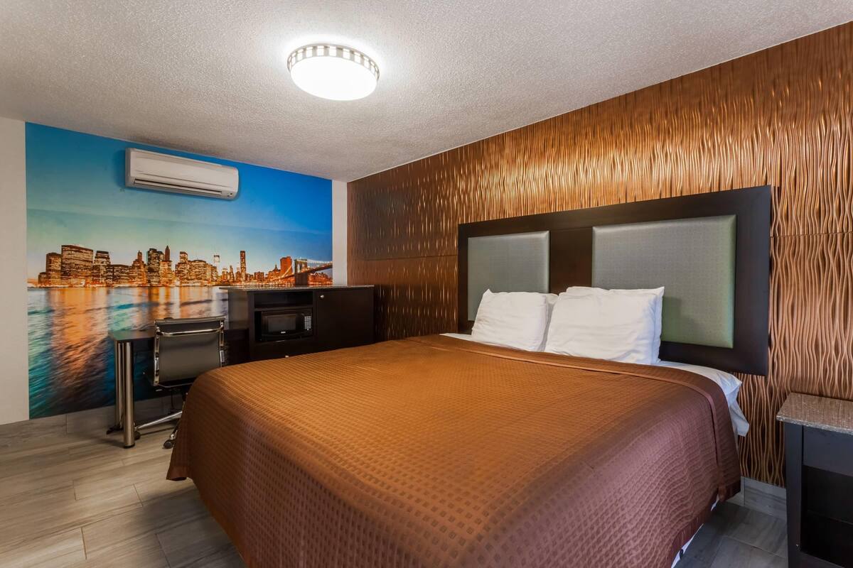 Una habitación de hotel con cama, escritorio, aire acondicionado y un mural con vistas a la ciudad.