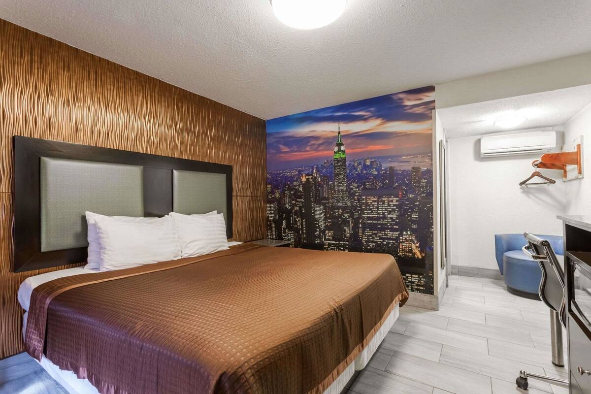 Habitación de hotel con una cama grande, un mural con vista a la ciudad, un escritorio con silla y un equipo de aire acondicionado.
