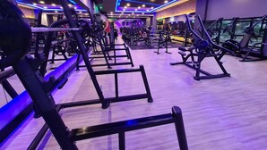 Ein Fitnessstudio mit unterschiedlichen Trainingsgeräten, darunter Kraftgeräte und Bänke, in blau-weißem Licht.