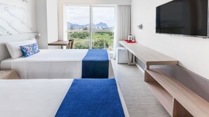 Ein Hotelzimmer mit zwei Betten, einem Fernseher, einem Schreibtisch und Blick ins Freie.