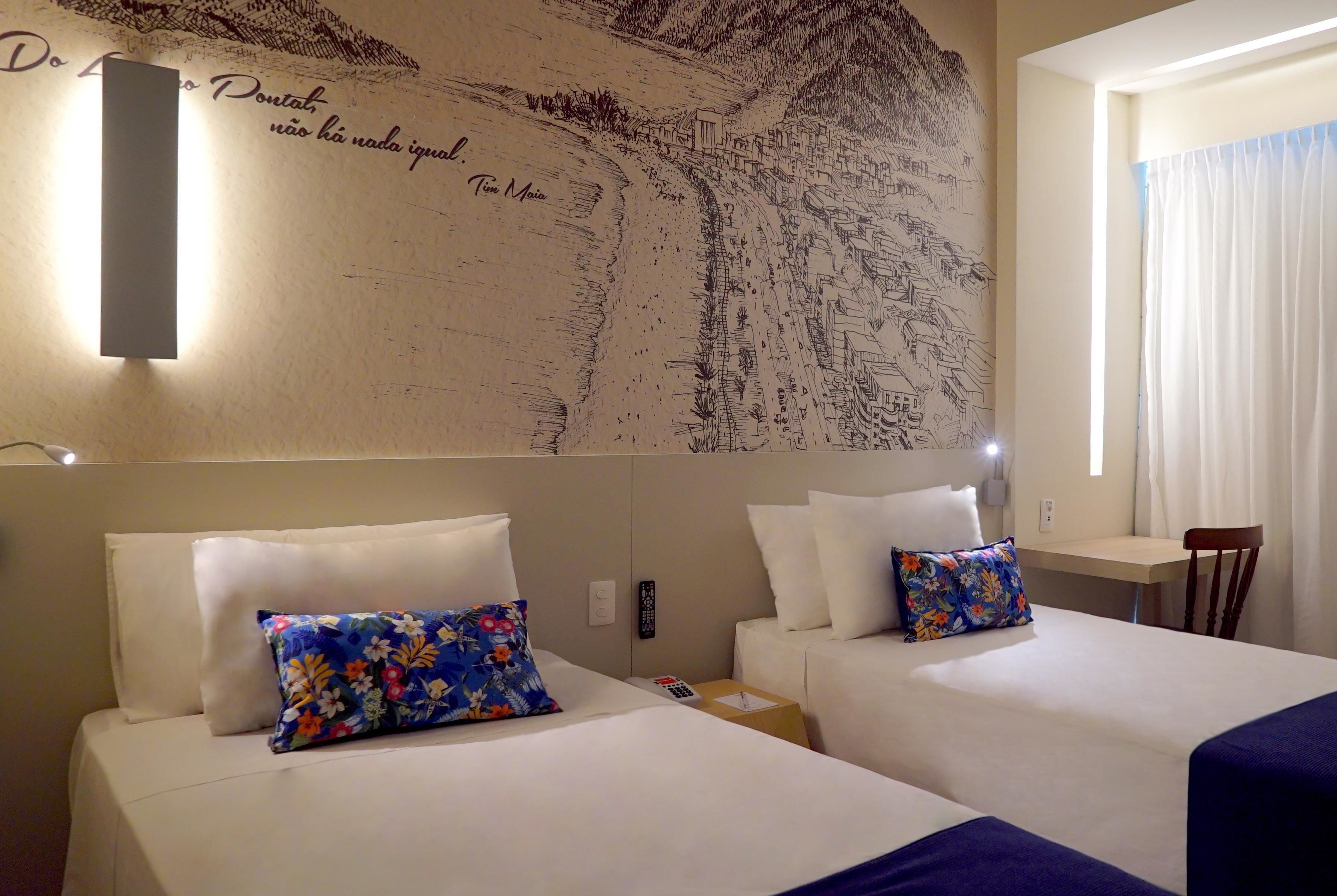 A hotel room with two beds, a wall mural, a small table, and a chair.
