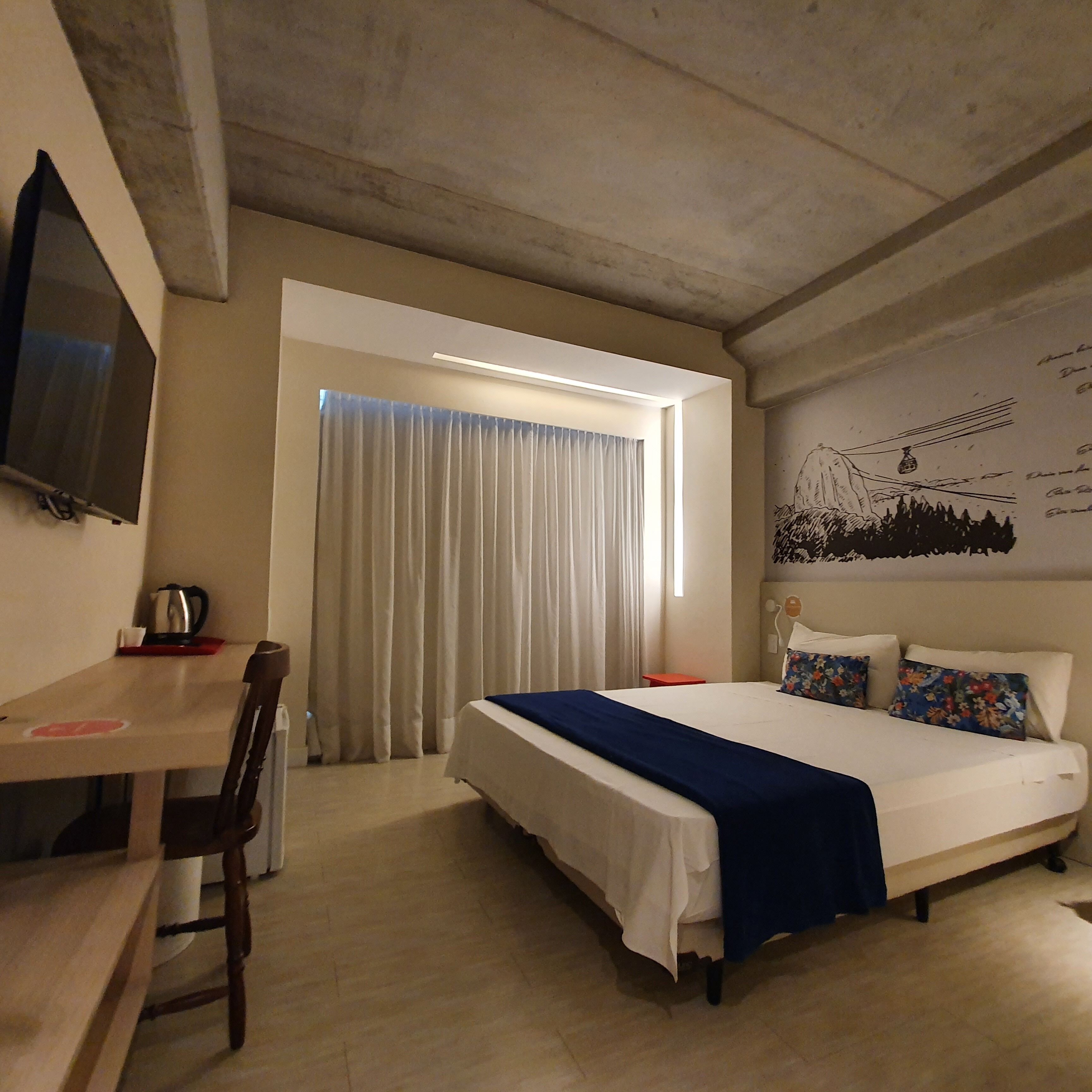 A hotel room with a bed, a desk, a chair, a television, and a window with curtains.