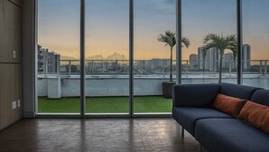 Ein modernes Wohnzimmer mit einem großen Schiebeglasfenster, das auf einen Balkon mit Blick auf Stadt und Berge führt.
