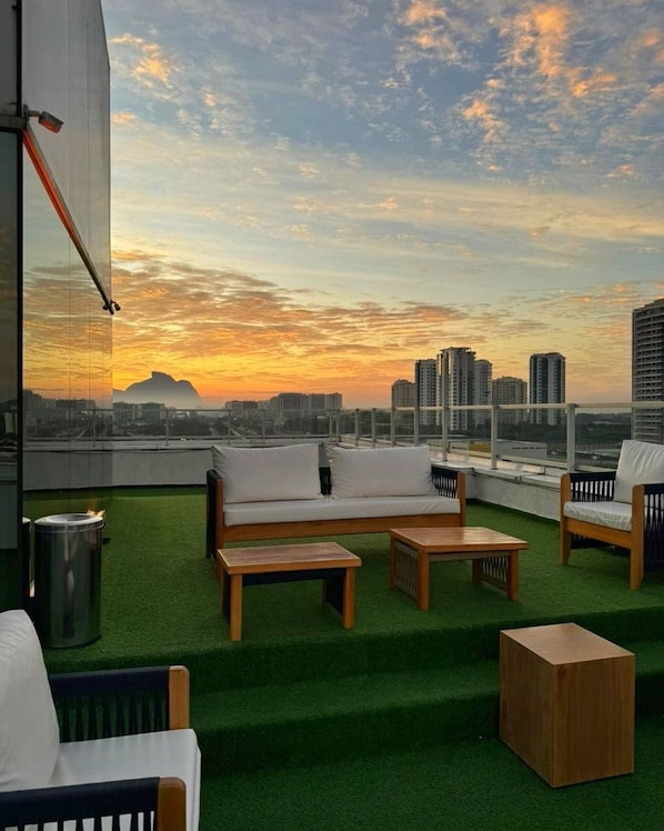 Terraza en la azotea con un sofá, sillas y una mesita, con vistas a un paisaje urbano al atardecer.