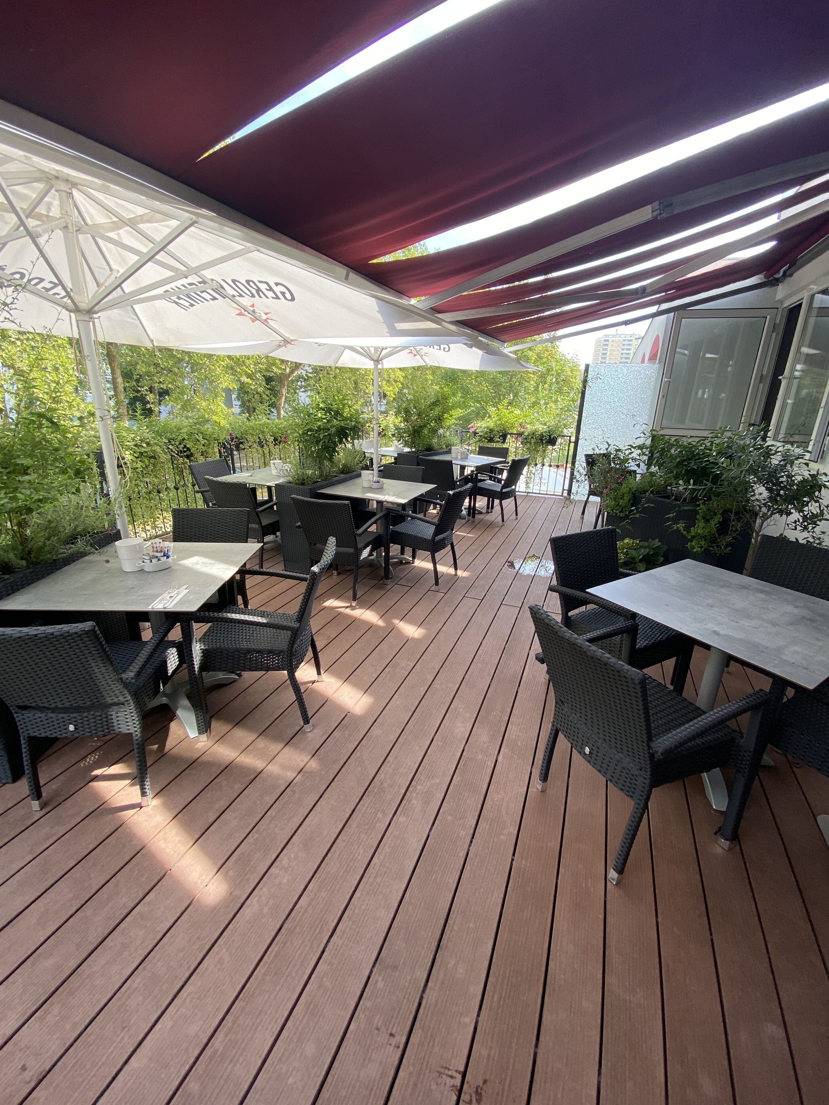 Une terrasse extérieure avec des tables et des chaises, protégée par des parasols et entourée de verdure.