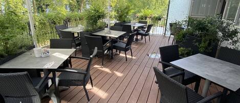 Une terrasse extérieure avec des tables et des chaises, protégée par des parasols et entourée de verdure.