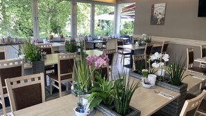 A restaurant with multiple tables and chairs, each adorned with potted plants and flowers. - Hotel am Westend (Lahr)