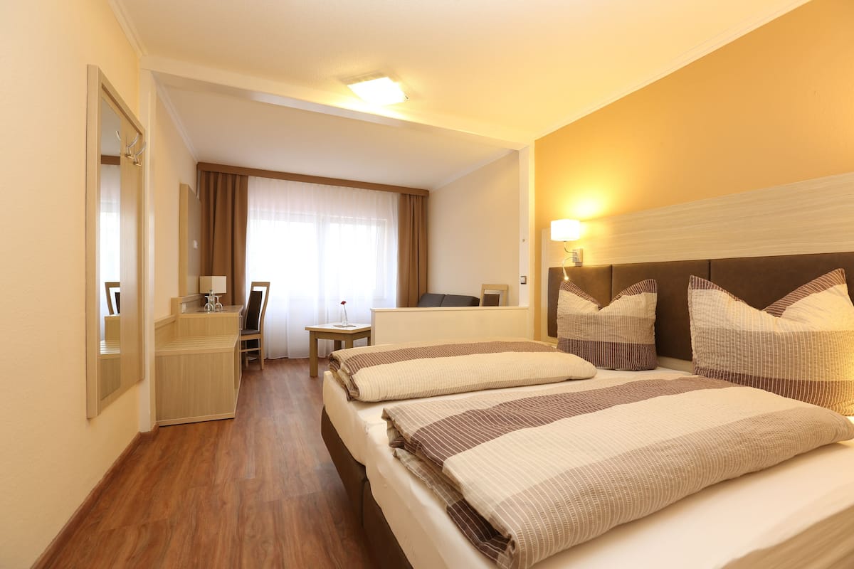 Quarto de hotel com duas camas, uma mesa, uma cadeira, um espelho e uma janela com cortinas.