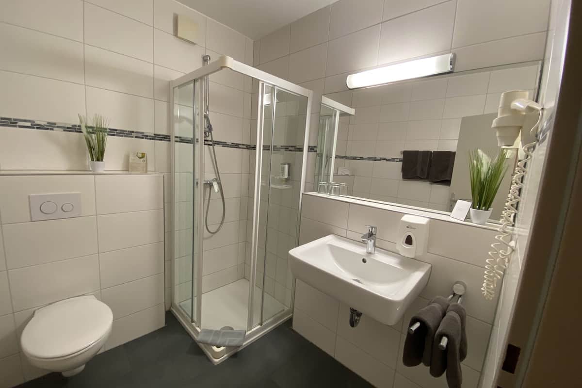 Uma casa de banho moderna com chuveiro envolto em vidro, uma sanita branca e uma lavatório.
