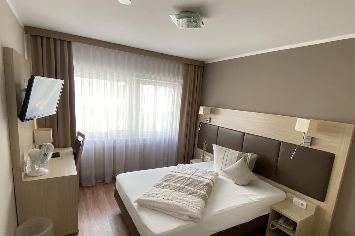 Quarto de hotel com cama, mesa de cabeceira, televisão e escrivaninha com cadeira.