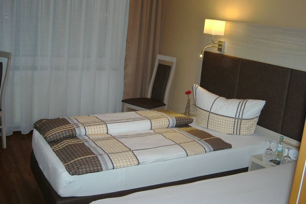 Quarto de hotel com cama, mesa de cabeceira, luminária e uma cadeira.