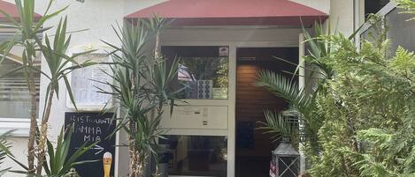 Un restaurante llamado 'Ristorante Pizzeria Mama Mia' con un toldo rojo y plantas en macetas al frente.