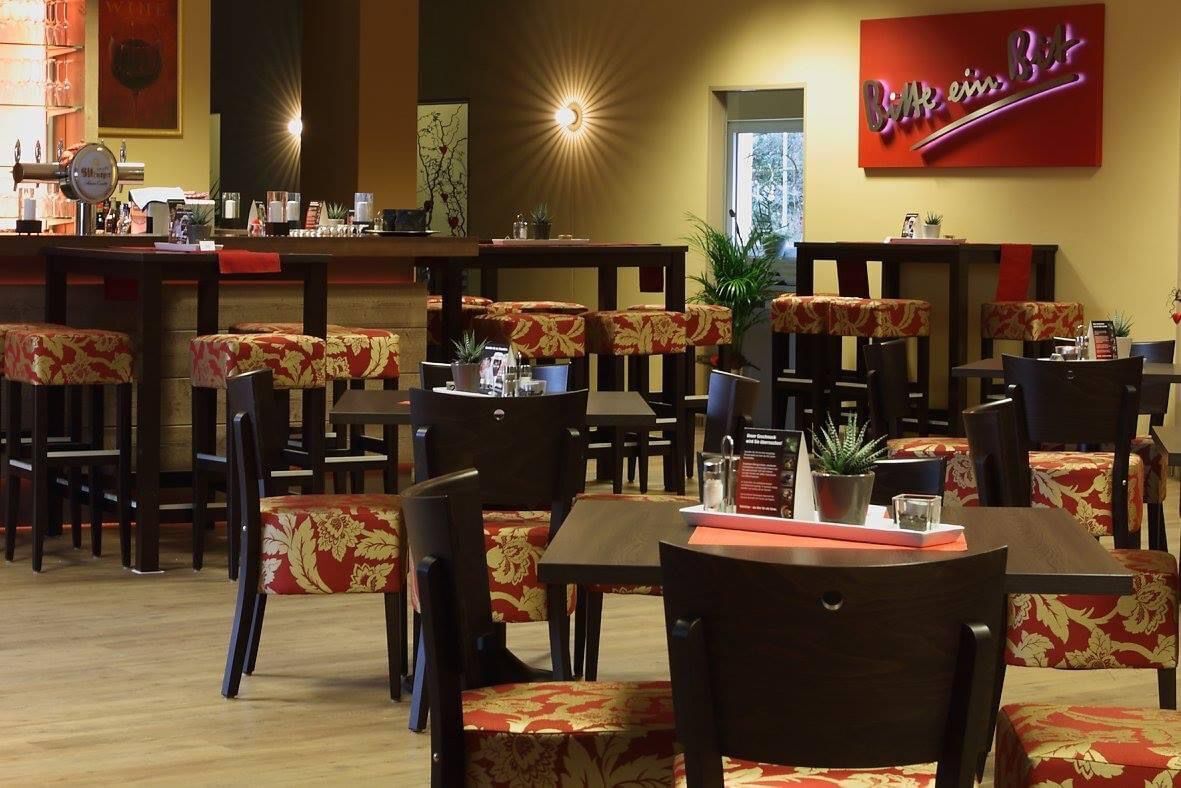 A restaurant interior with booths and tables, a bar area, and a red sign on the wall.