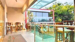 A hotel lobby with wooden chairs and tables, a glass railing, and a view of greenery outside. - Hotel Arujá (Aruja)