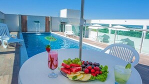Ein Tisch am Pool mit einer Obstplatte, einem rosafarbenen Getränk und einem grünen Cocktail.