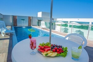 Mesa à beira da piscina com um prato de frutas, uma bebida rosa e um cocktail verde.