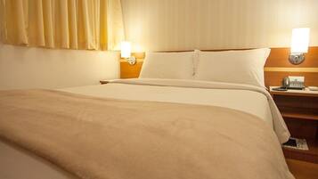 Una habitación de hotel con una cama grande, una mesita de noche con lámpara y un teléfono.