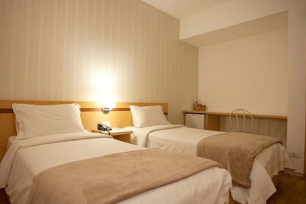 Una habitación de hotel con dos camas, una mesita de noche con lámpara, una pequeña mesa y una silla.