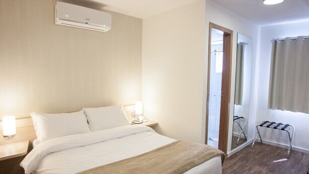Ein Hotelzimmer mit Bett, Nachttischlampen, einem Spiegel, einem Fenster mit Vorhängen und einer Klimaanlage.