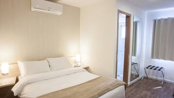 Une chambre d’hôtel équipée d’un lit, de lampes de chevet, d’un miroir, d’une fenêtre avec des rideaux et d’un appareil de climatisation.