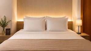 A neatly made bed with a headboard, a bedside table with a lamp, and a small vase with flowers. - Hotel Arujá (Aruja)