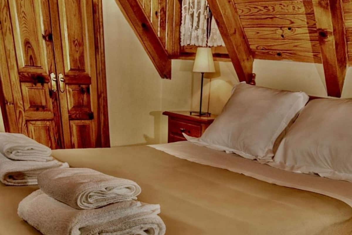 Habitación de hotel con techo de madera, cama con ropa blanca y mesita de noche con lámpara.