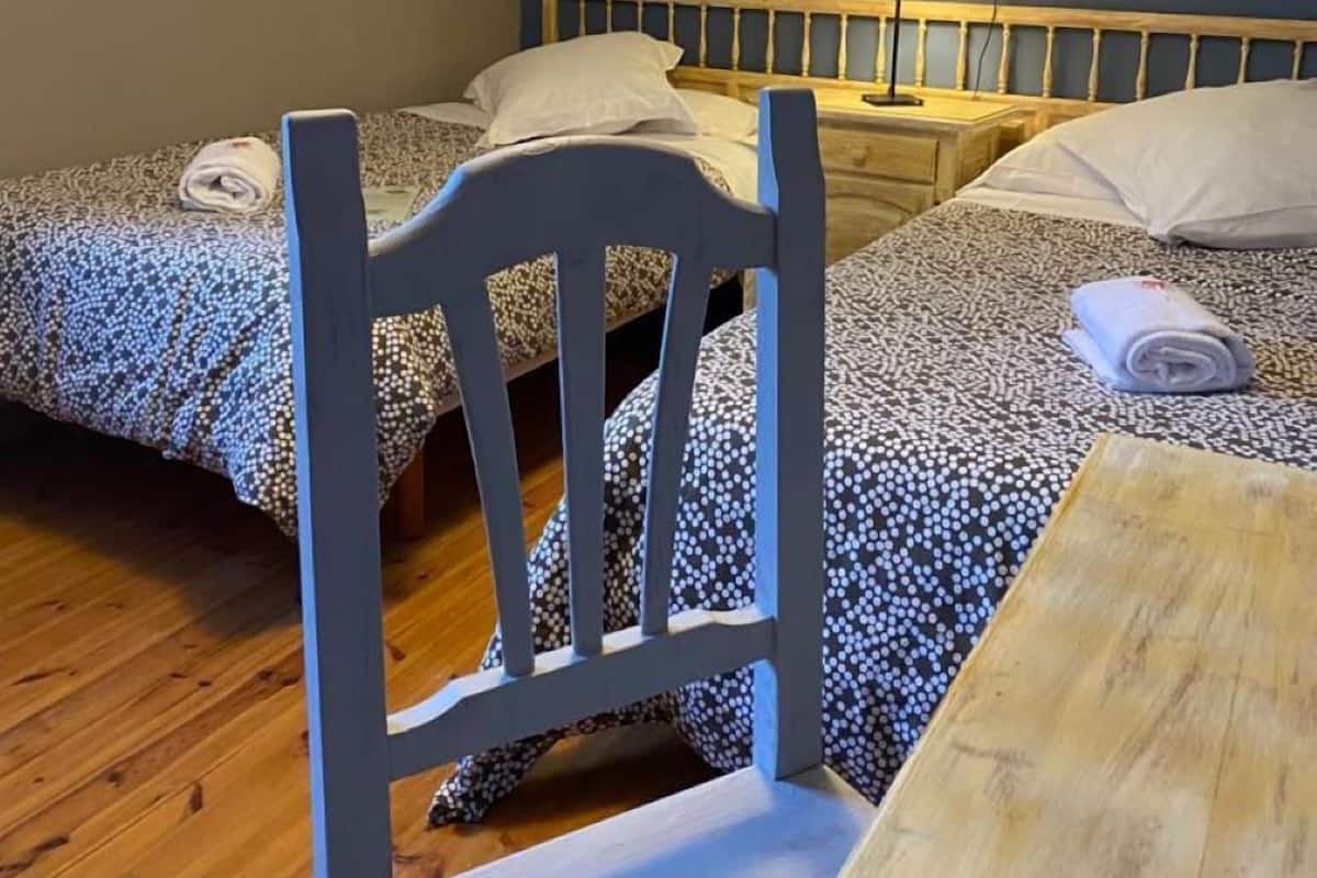 Un dormitorio con dos camas, una silla de madera, una mesa y una lámpara de noche.