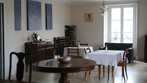 A dining area with a round wooden table, chairs, a wine rack, and a chandelier. - Le Voltaire Chambres et Table d'Hotes (Airvault)