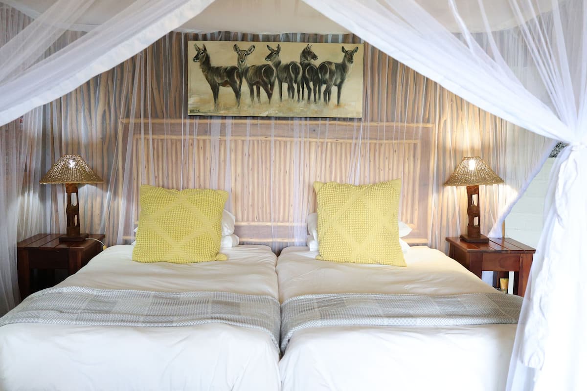 A double bed with two yellow pillows, a canopy, and a painting of deer on the wall.