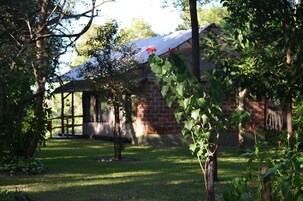 Un edificio de ladrillo con un porche cubierto y un jardín con follaje verde y una flor roja.