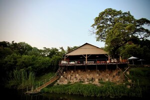 Un edificio junto al río con una terraza techada y una escalera que lleva a una plataforma.