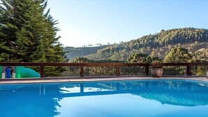 Una piscina con cubierta de madera, rodeada de árboles y un paisaje montañoso al fondo.