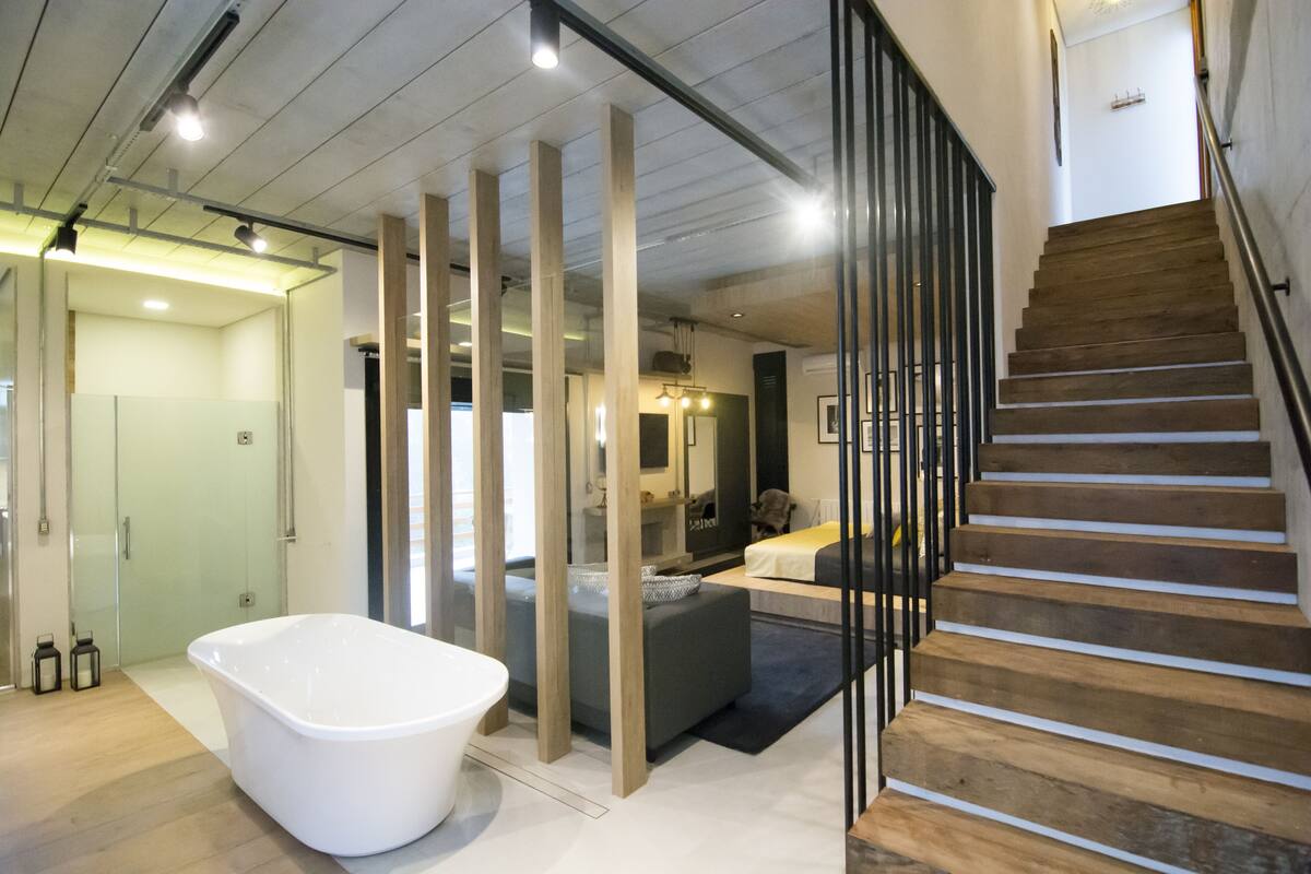 Une salle de bain moderne avec une baignoire sur pieds, un plancher en bois et un escalier avec des éléments en bois.