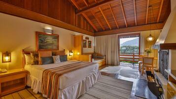 Une chambre spacieuse avec un grand lit, des poutres apparentes en bois au plafond, un balcon avec vue et une cheminée.
