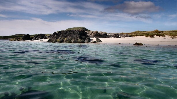Helder turquoise zeewater met zichtbare rotsen en een zandstrand.