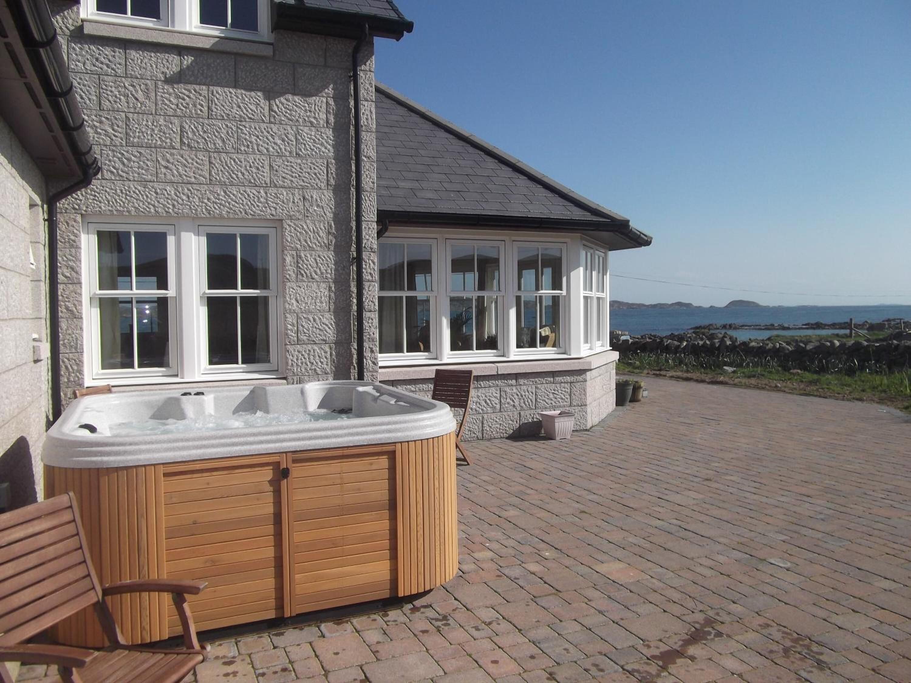 A stone building with a hot tub, wooden chairs, and a view of the sea.