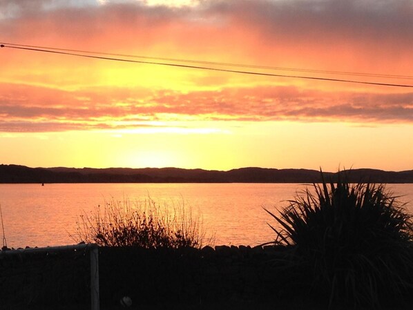 A sunset over a body of water with a stone wall and vegetation in the foreground.