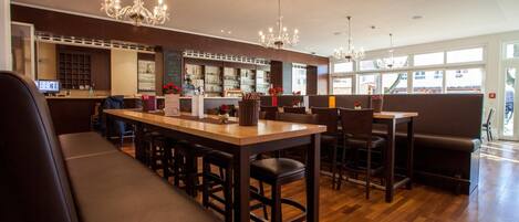 A modern bar area with a long counter, bar stools, and a seating area with a bench and cushioned chairs.
