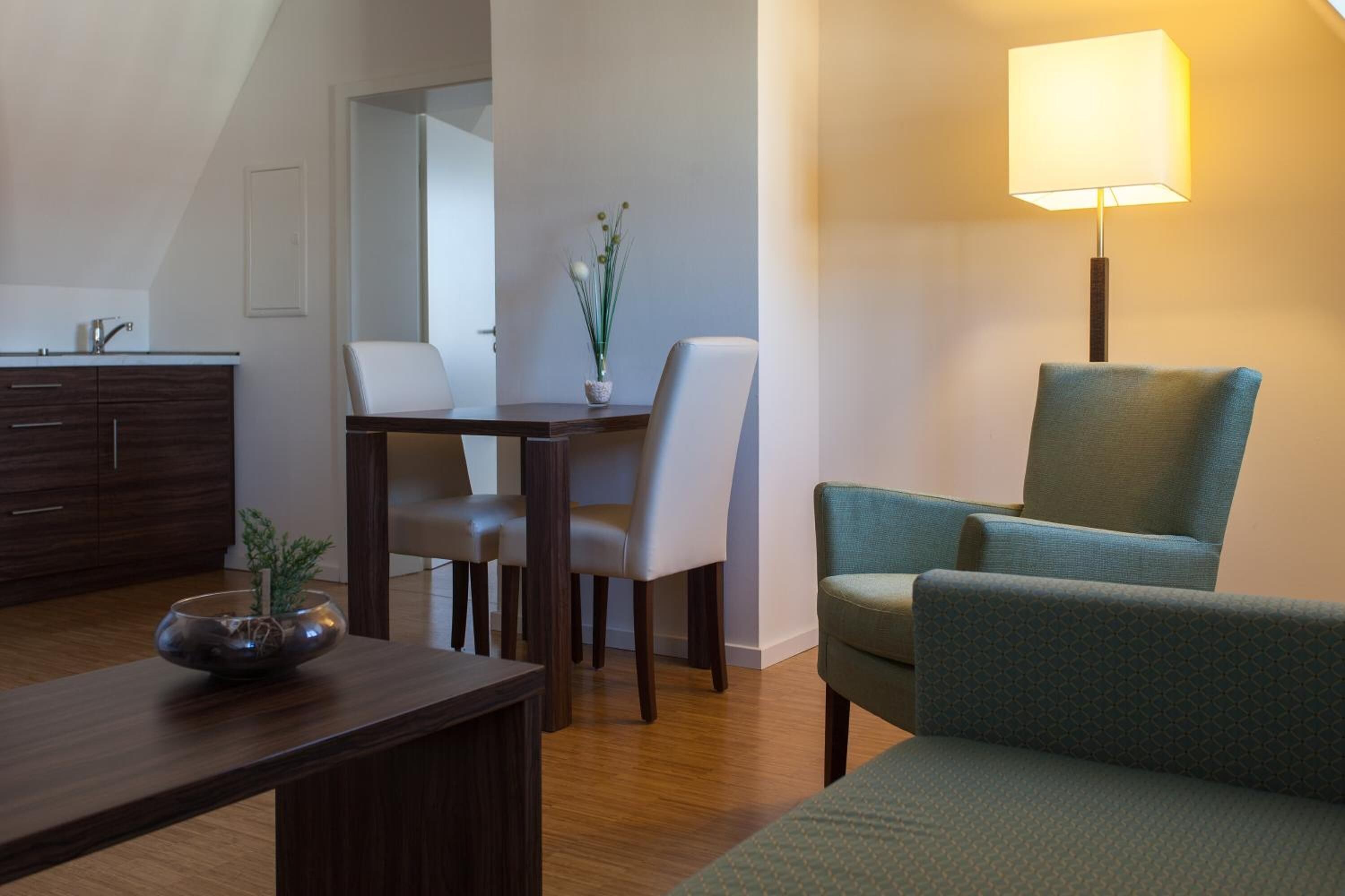 Una sala moderna con una mesa de comedor, dos sillas, un sofá, una lámpara y una planta pequeña sobre la mesa.