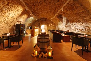 Un interior rústico con paredes de piedra, muebles de madera y una barrica central. Se han dispuesto mesas y sillas para comer.