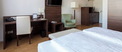 A hotel room with a desk, chair, TV, lamp, and two beds.