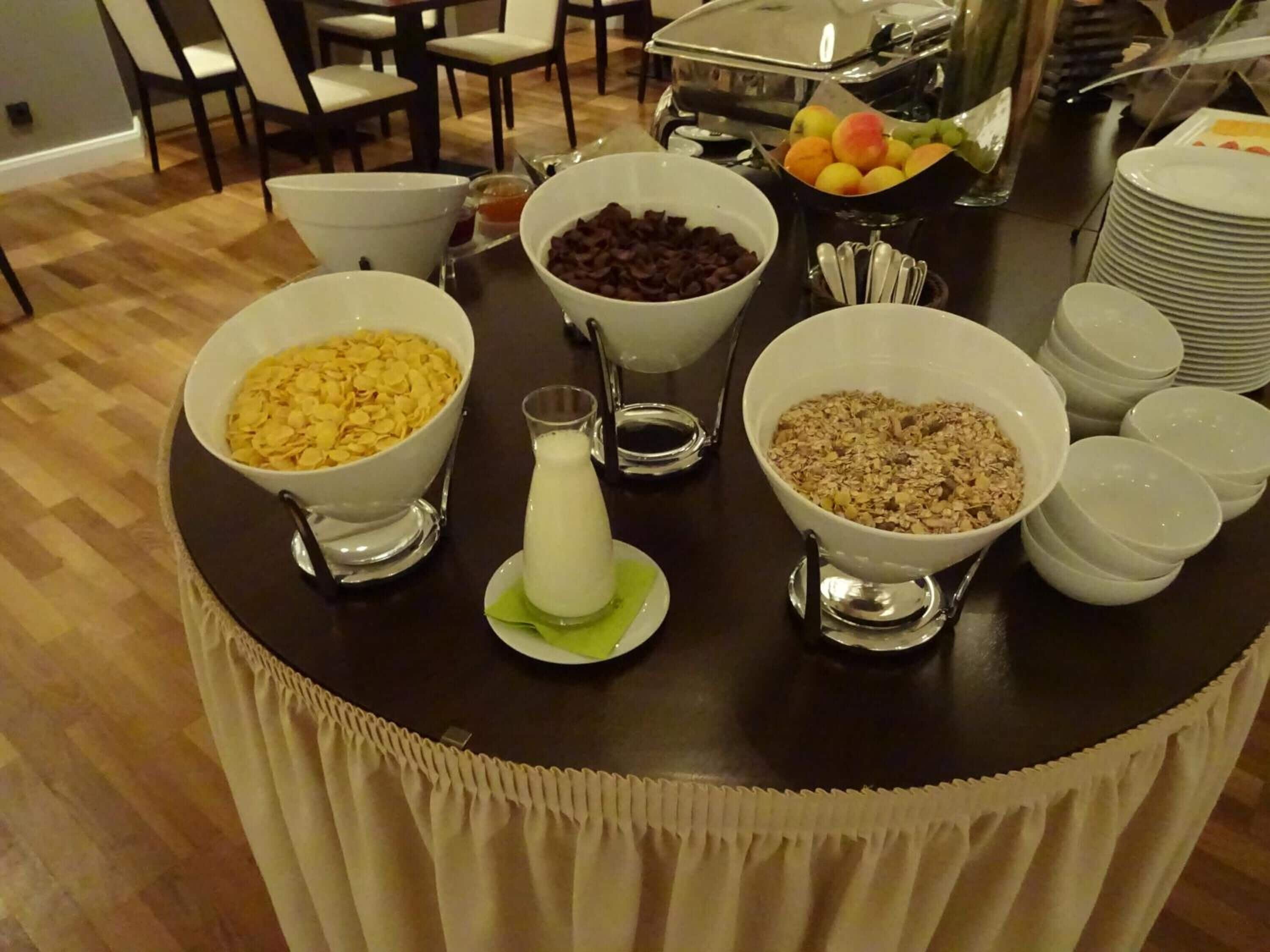 Un bufé de desayuno con tazones de cereales, leche y frutas.