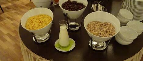 Un bufé de desayuno con tazones de cereales, leche y frutas.