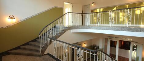 Un interior de varios niveles con una escalera central, una zona de recepción y un bar-salón.
