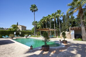 A pool area with lounge chairs, a pergola, and potted plants.