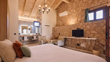 A bedroom with a large bed, a TV mounted on a stone wall, and a wooden ceiling.