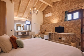 A bedroom with a large bed, a TV mounted on a stone wall, and a wooden ceiling. - S'Hort de Son Caulelles - Adults Only (Marratxi)