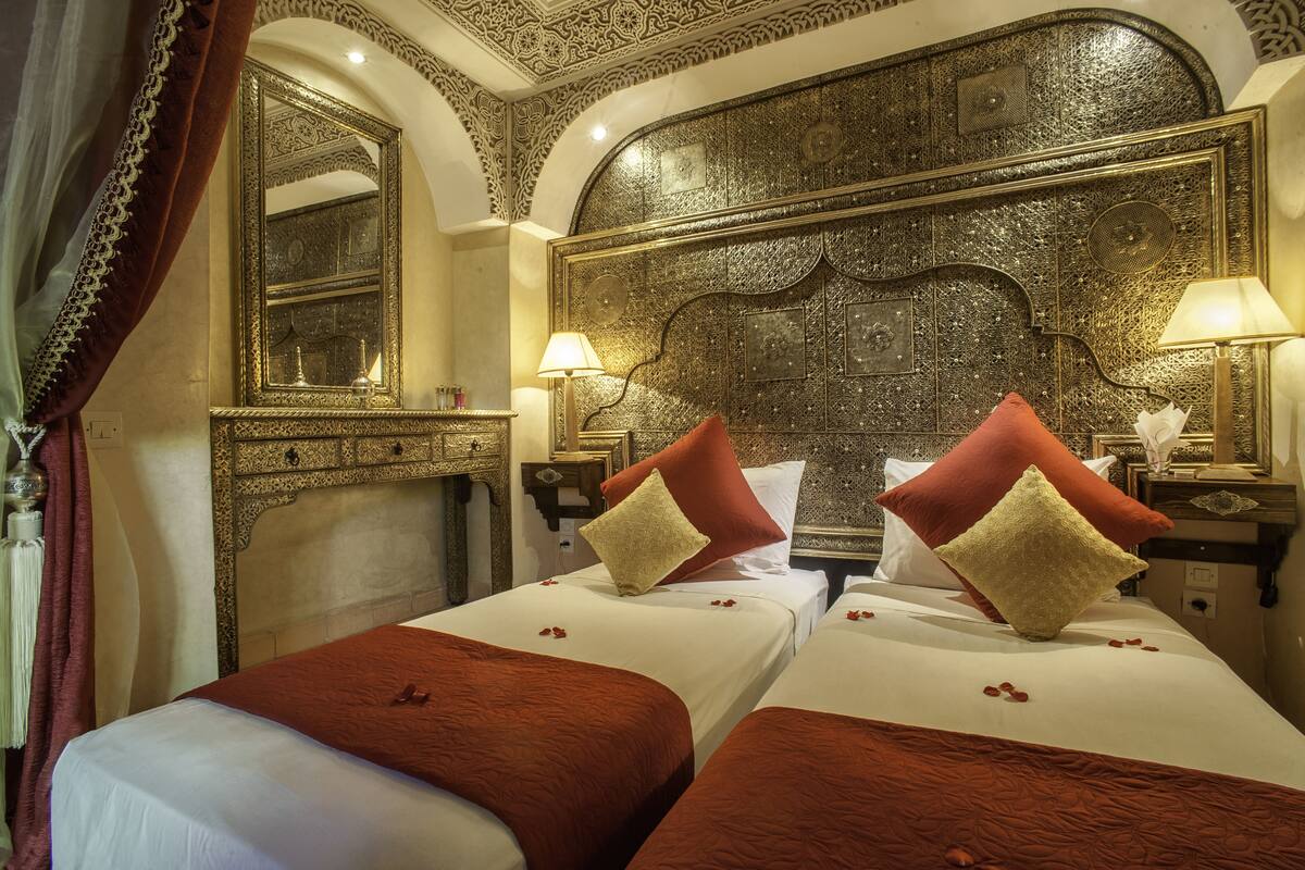 A hotel room with two beds, ornate headboard, and a large mirror.