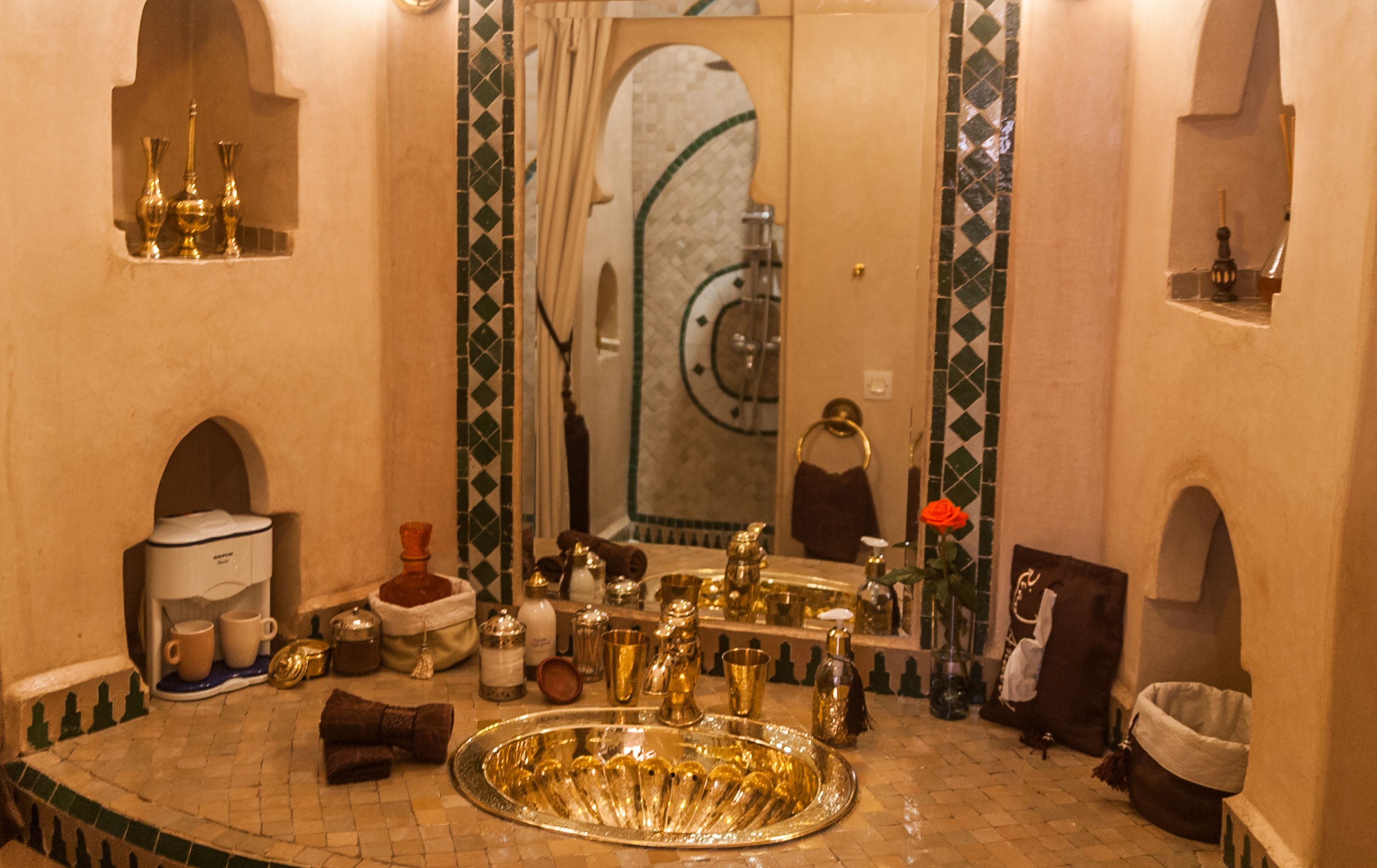 A traditional bathroom with a large, ornate sink, multiple gold-colored vessels, and a mirror with a decorative frame.