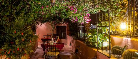 An outdoor dining area with a table and chairs, surrounded by lush greenery and flowering plants.